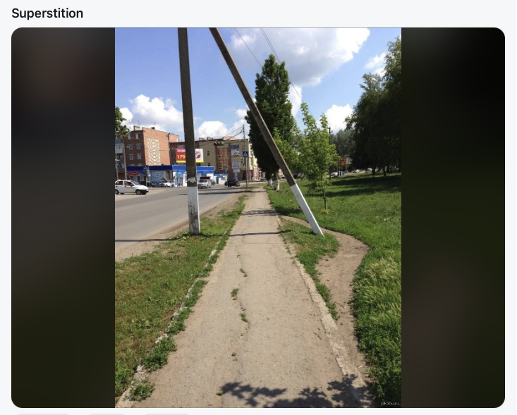 A worn dirt path leaving the sidewalk to avoid walking under a leaning utility pole.